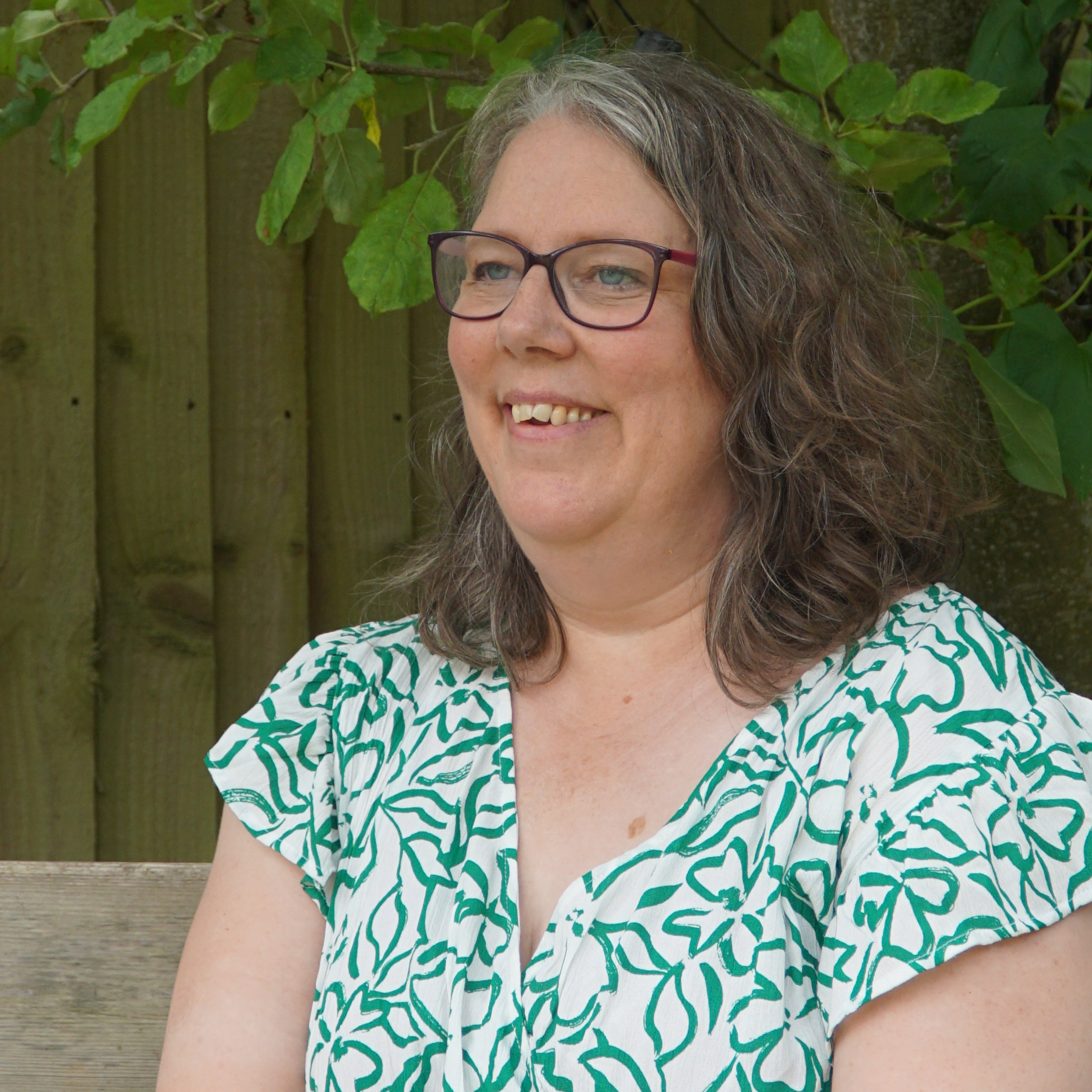 Person wearing a green and white patterned dress lying on the ground with plants around.